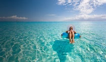 Woman sitting in an inflatable ring in the shallow waters of the sea with a yacht in the distance