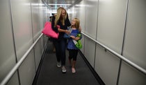 Woman walking with her arm around a child down an airbridge to board an aircraft
