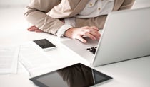 Woman sitting at a white desk with tablet and mobile phone while working on a laptop