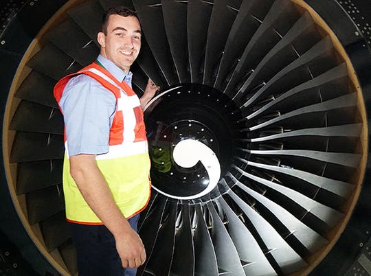 Aircraft engineer standing in front of an engine smiling