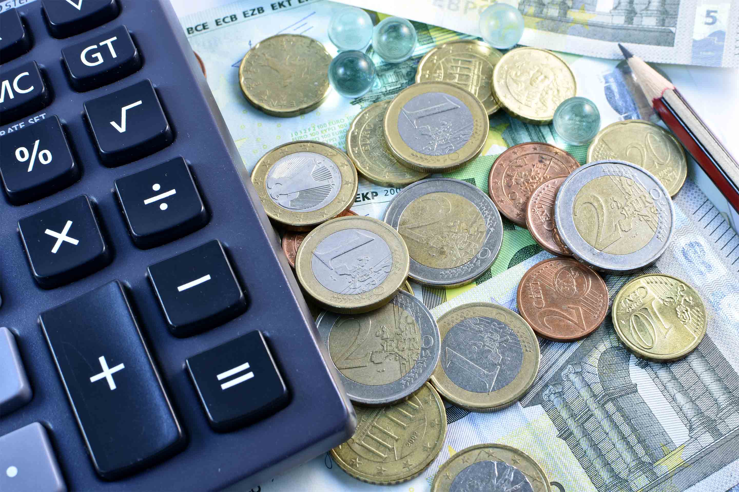 Close up of Euro coins and notes beside a calculator and a pencil