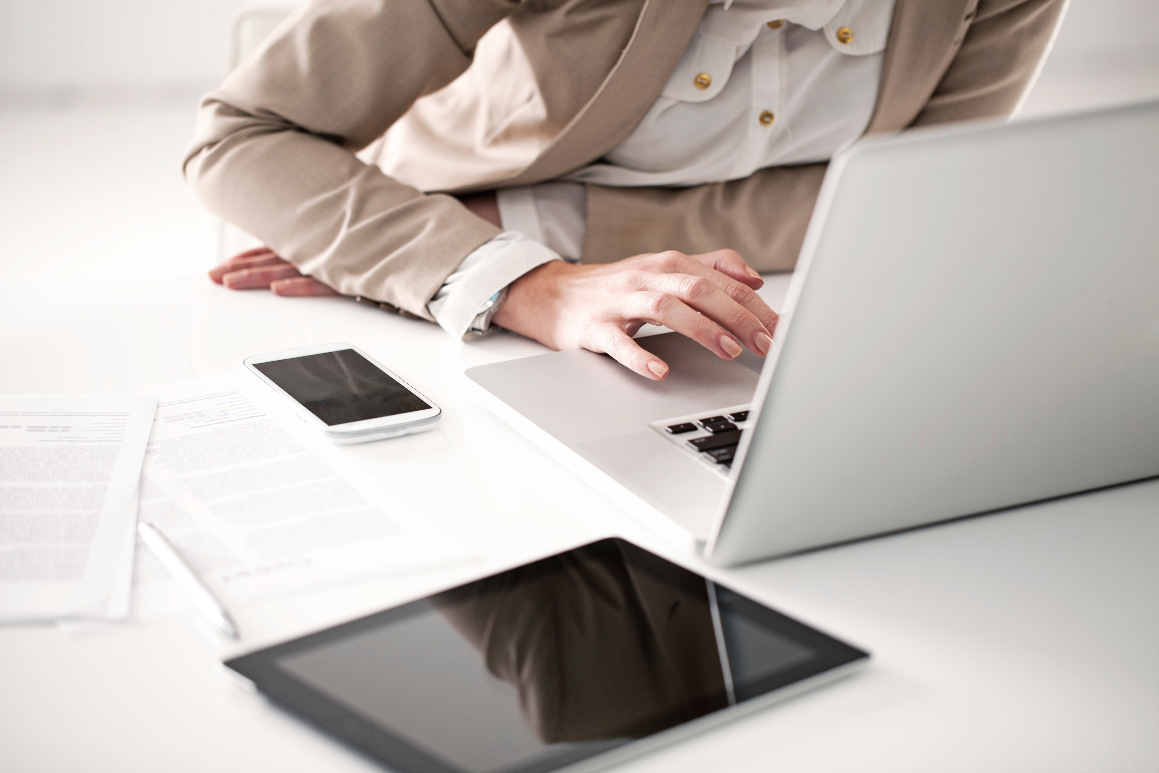 Woman sitting at a white desk with tablet and mobile phone while working on a laptop