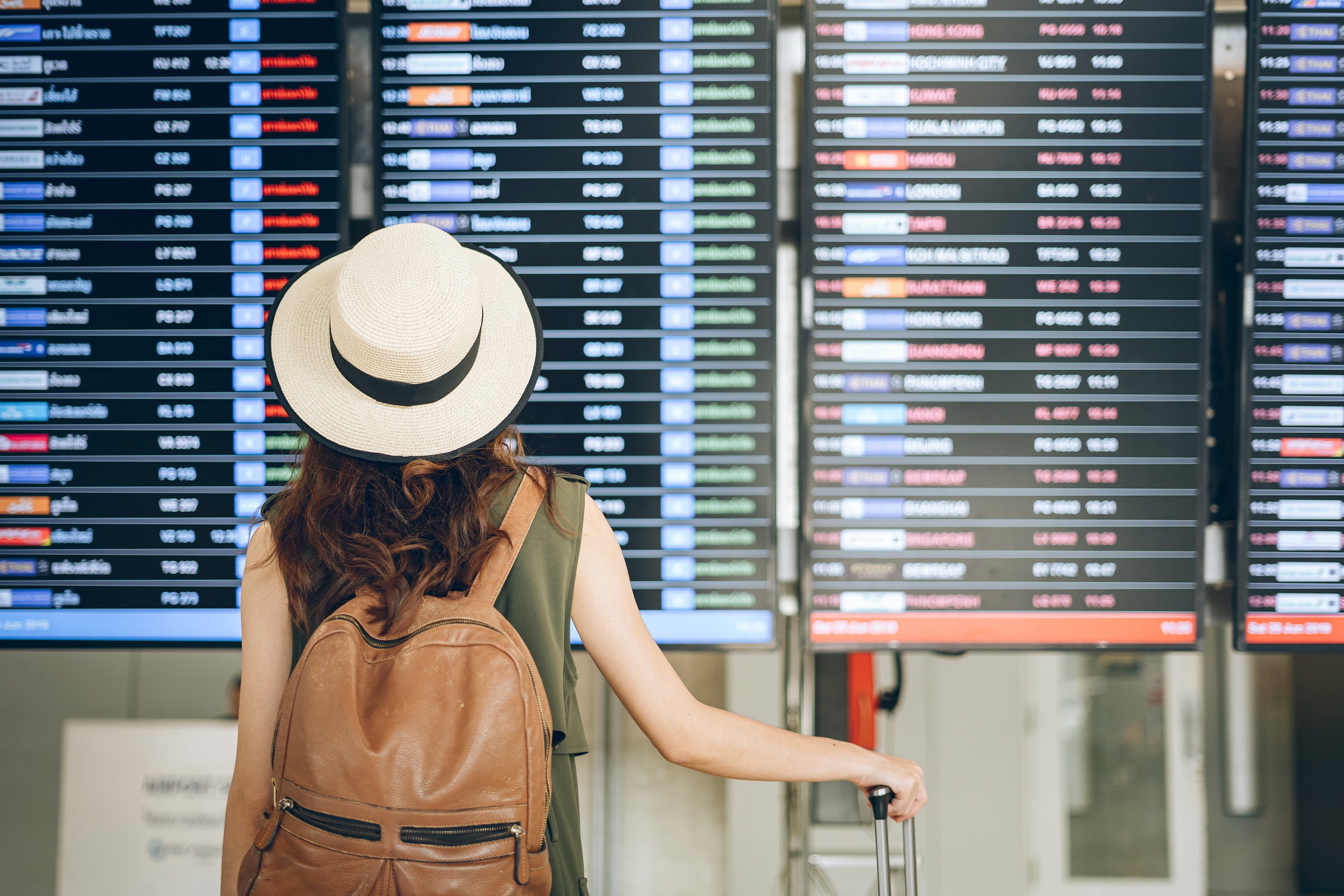 Rear view of a woman standing beside her luggage looking at airport notice board