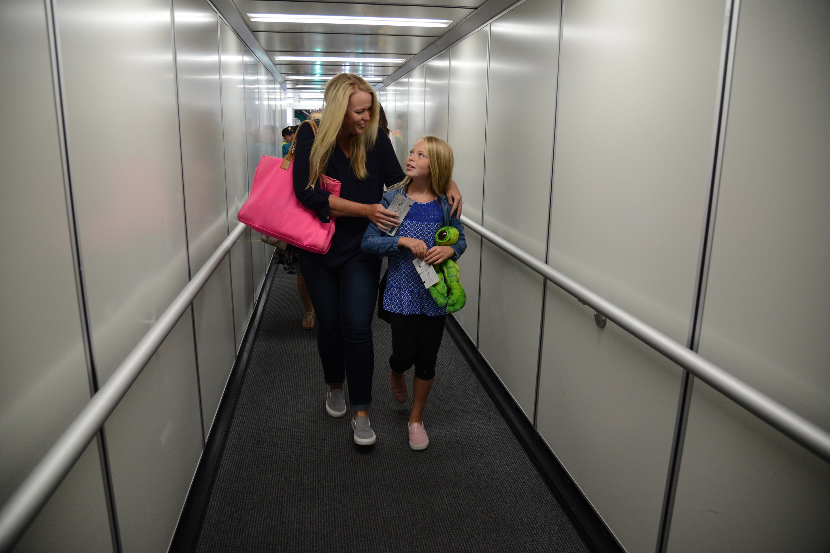Woman walking with her arm around a child down an airbridge to board an aircraft